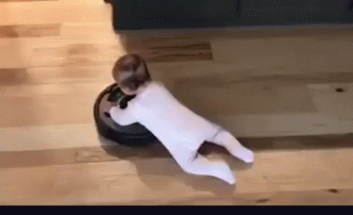 Young baby clings to a Roomba which drags it around room.
